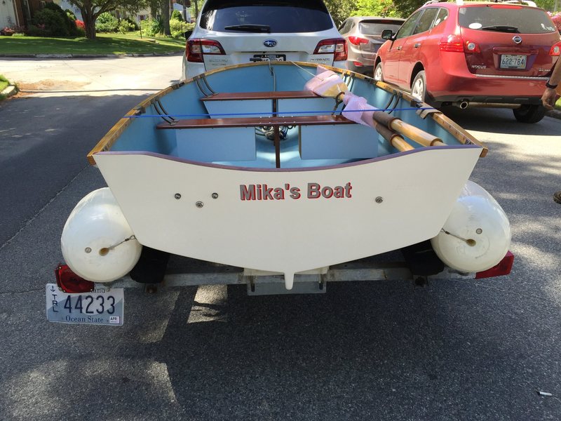 A wooden dinghy on its trailer with "Mika's Boat" painted across the transom